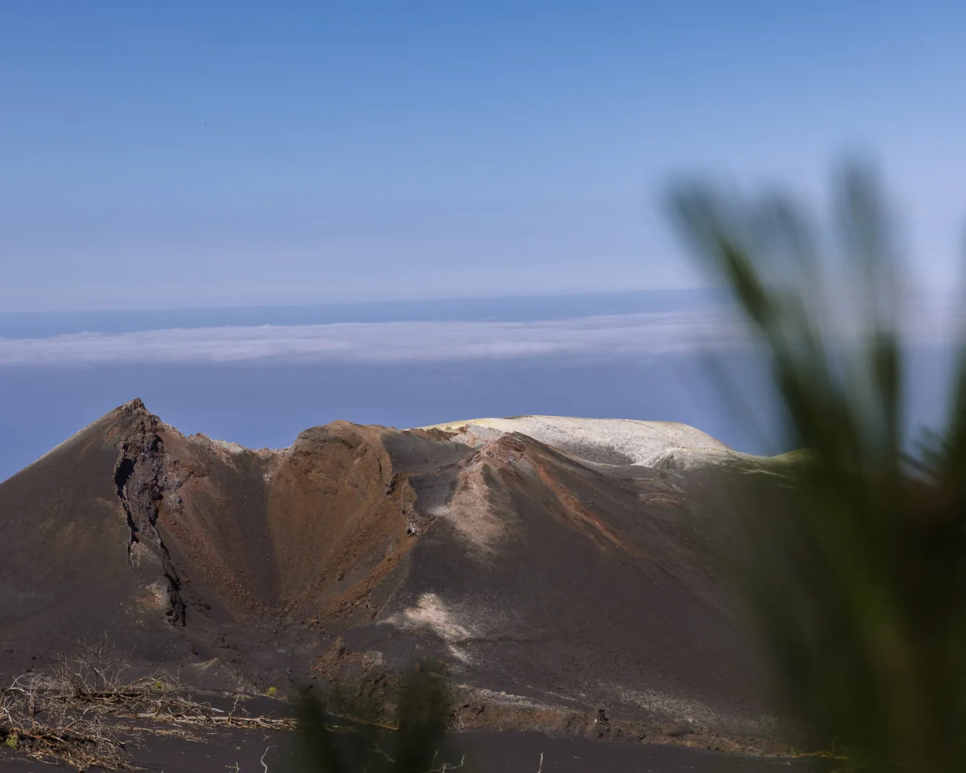 Volcanic crater landscape on La Palma in the Canary Islands, with rugged dark slopes, a pale ridge, and ocean clouds in the distance.