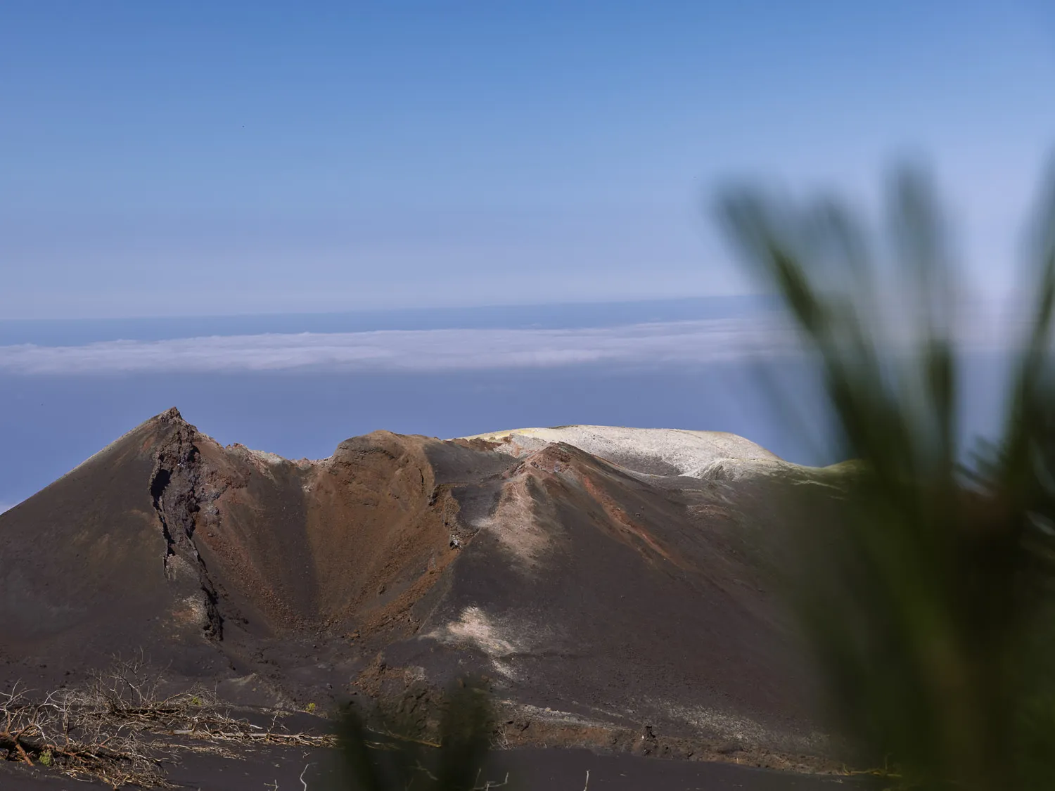 Volcanic crater landscape on La Palma in the Canary Islands, with rugged dark slopes, a pale ridge, and ocean clouds in the distance.