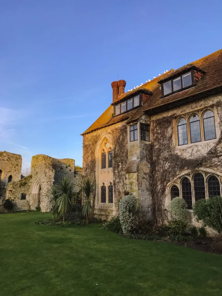 Stone manor house with mullioned windows and ivy, next to a ruined castle wall and lawn at Amberley Castle