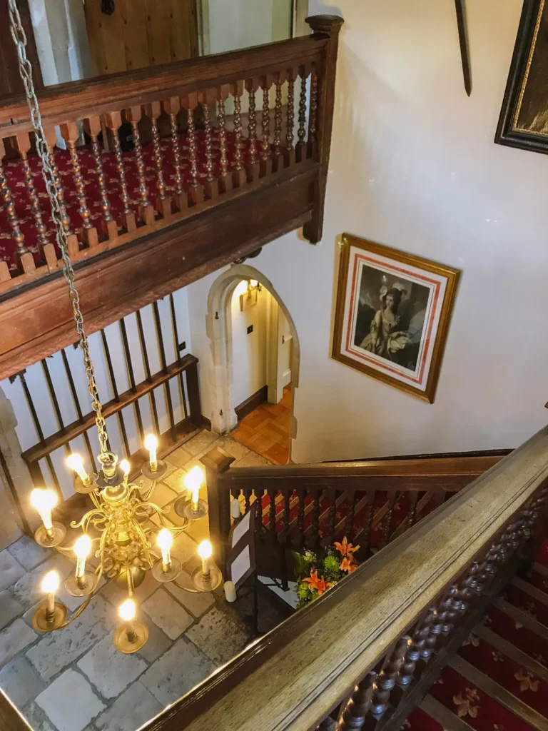 Carved oak staircase and brass chandelier looking down onto a stone-floored landing at Amberley Castle
