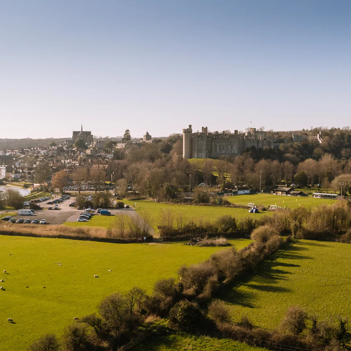 Drone view over Arundel with sheep grazing in fields, the castle and cathedral rising above the town and River Arun
