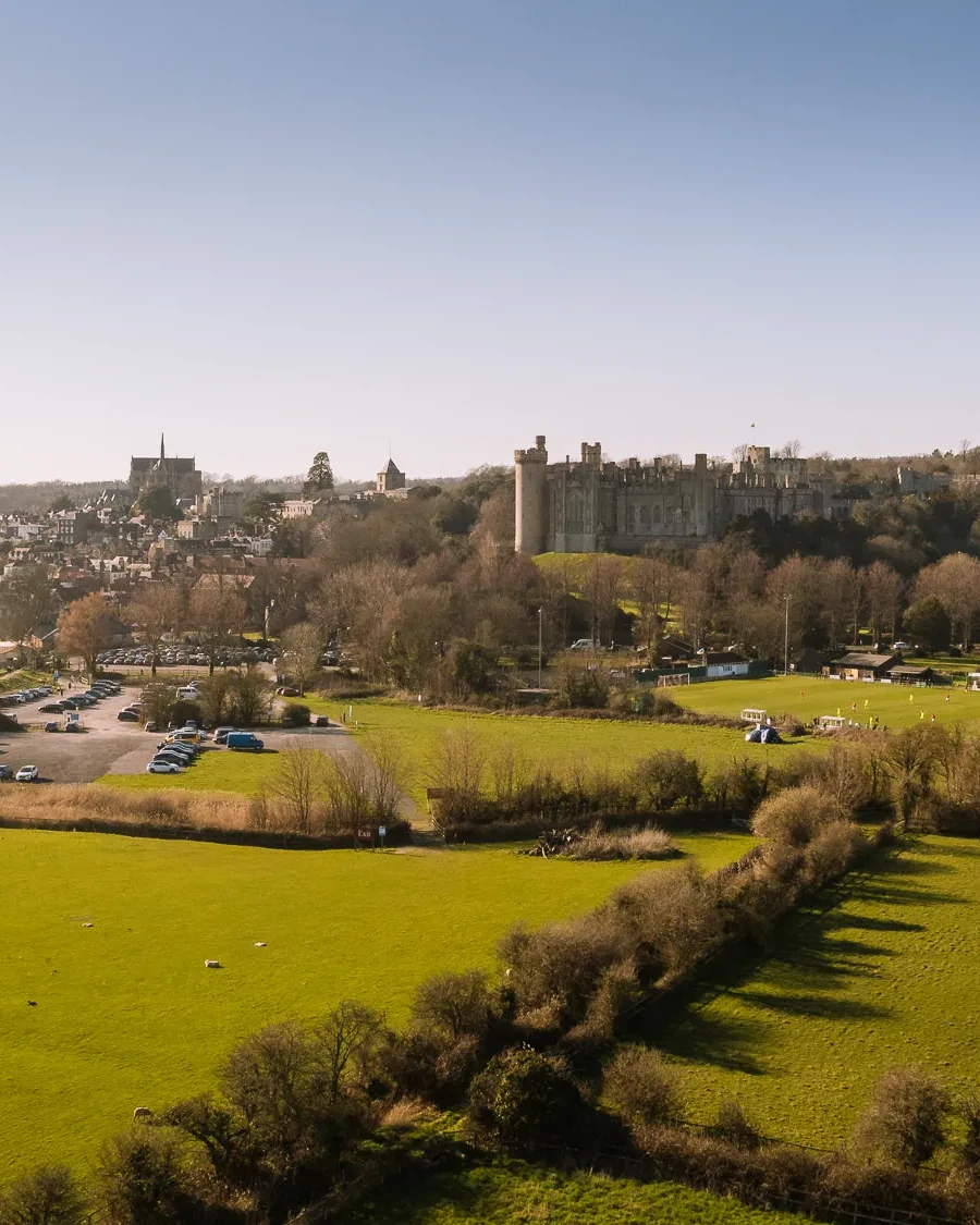 Drone view over Arundel with sheep grazing in fields, the castle and cathedral rising above the town and River Arun