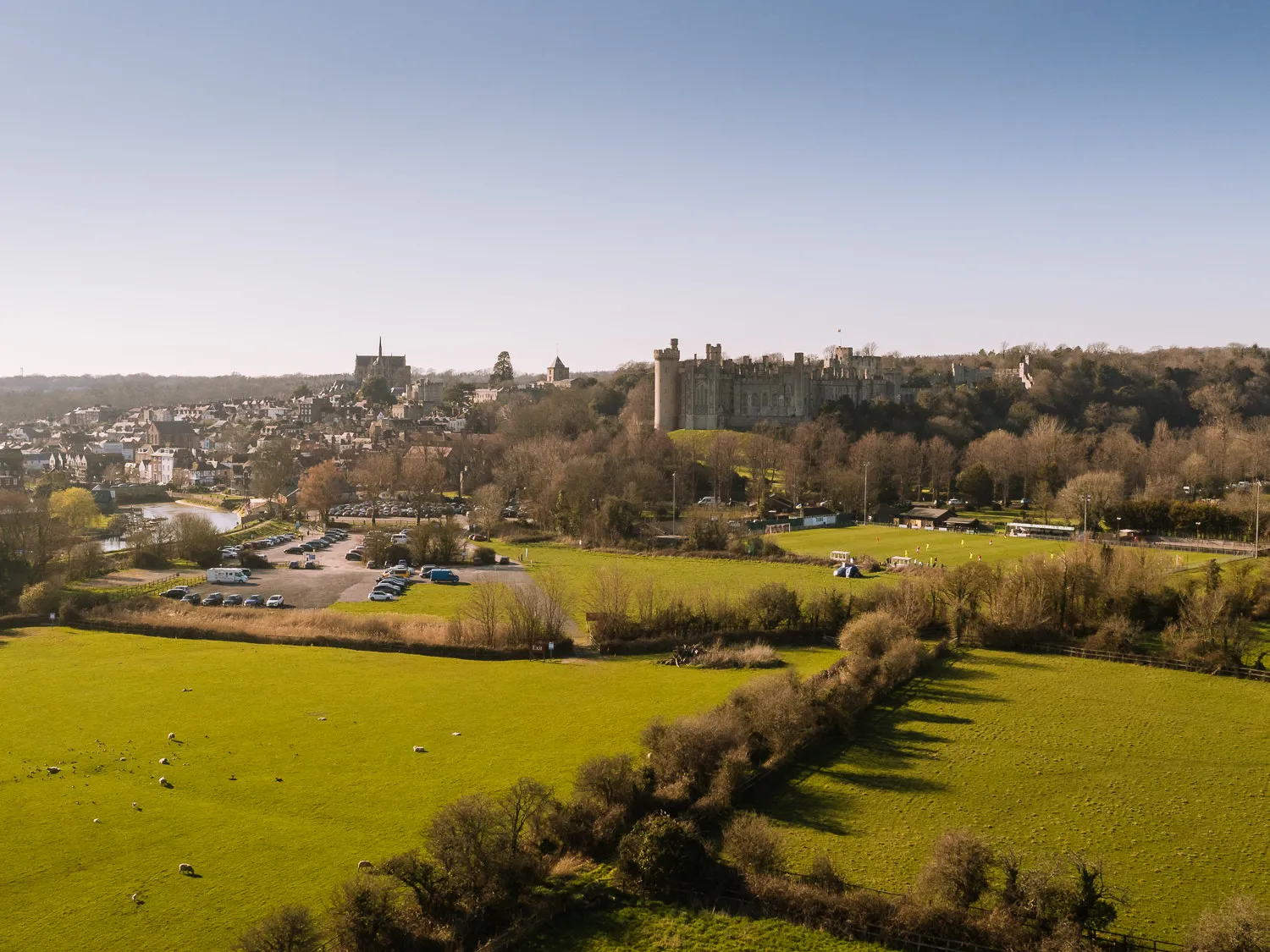 Drone view over Arundel with sheep grazing in fields, the castle and cathedral rising above the town and River Arun