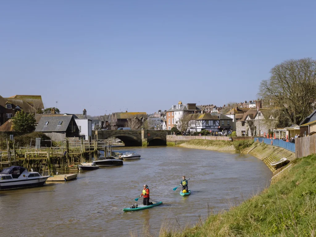 Two paddleboarders on the River Arun with Arundel's stone bridge and riverside houses behind them