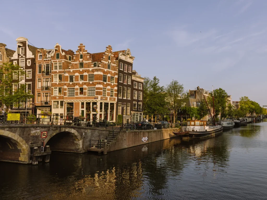 Historic canal houses, moored boats and a brick bridge beside a central Amsterdam canal