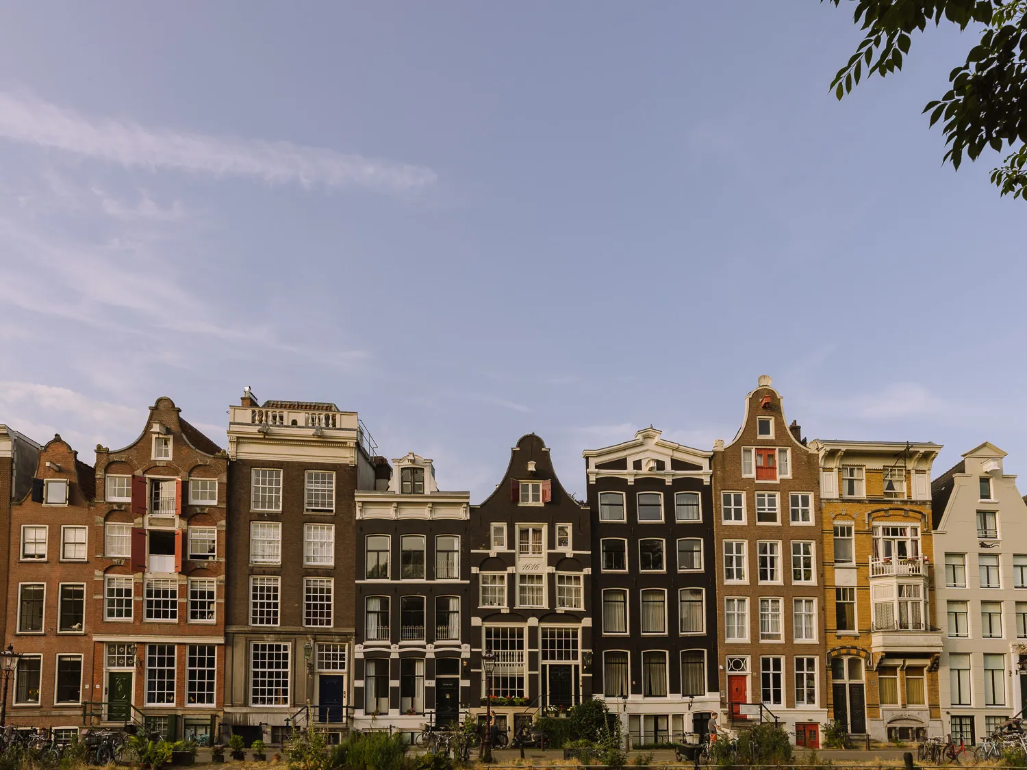 Historic Amsterdam canal houses and leafy trees reflected in calm water on a sunny evening