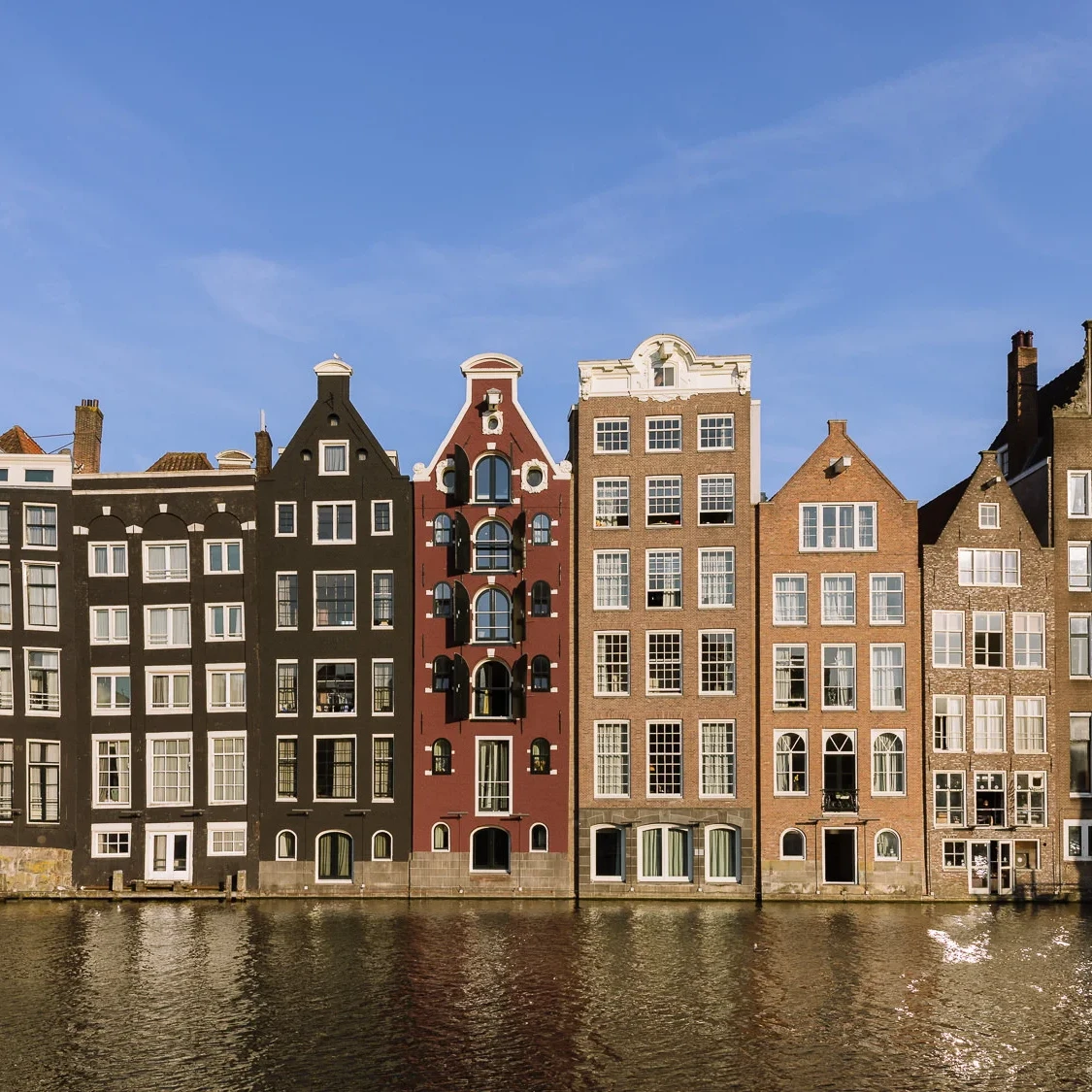 Row of narrow historic canal houses along a waterfront in Amsterdam