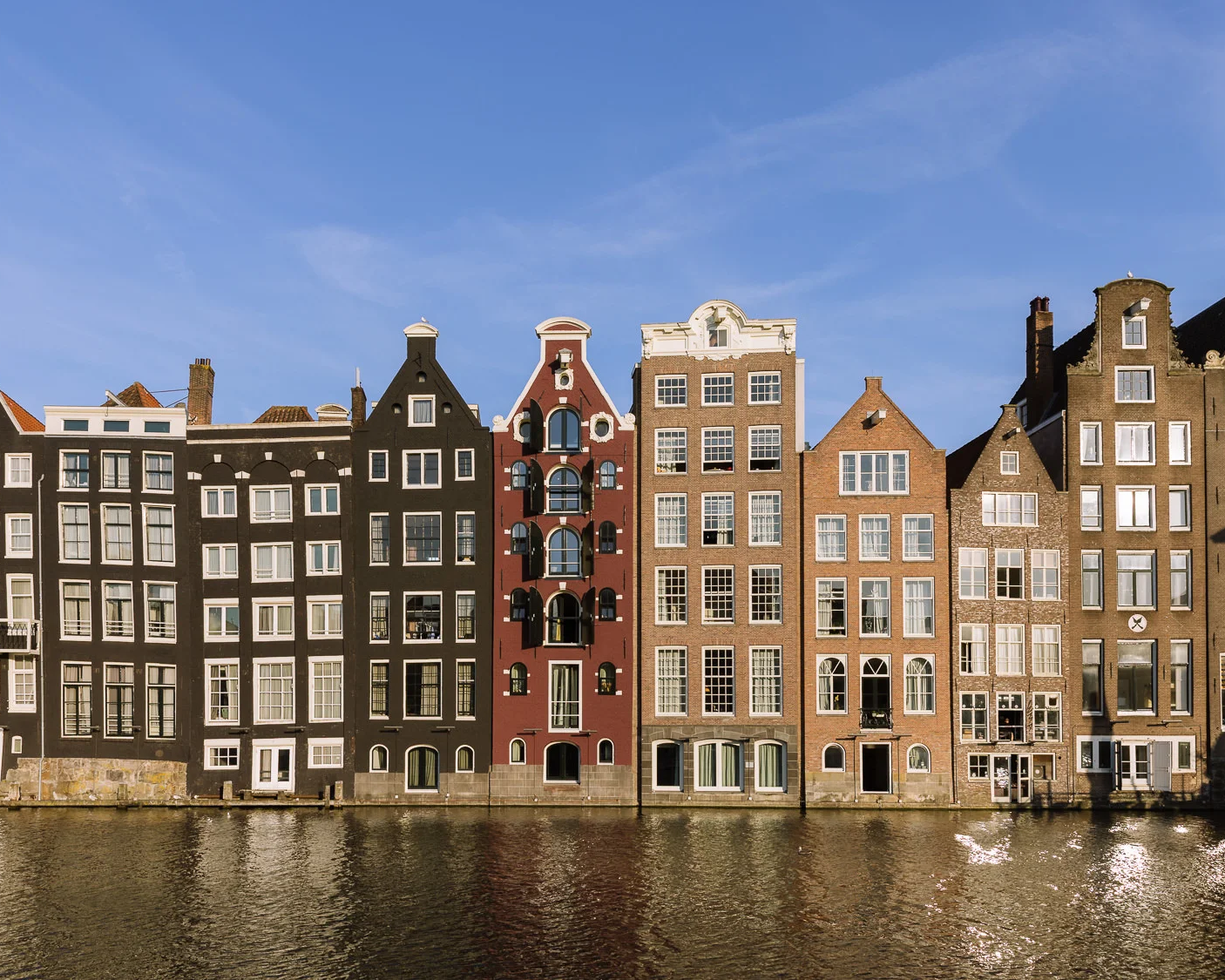 Row of narrow historic canal houses along a waterfront in Amsterdam