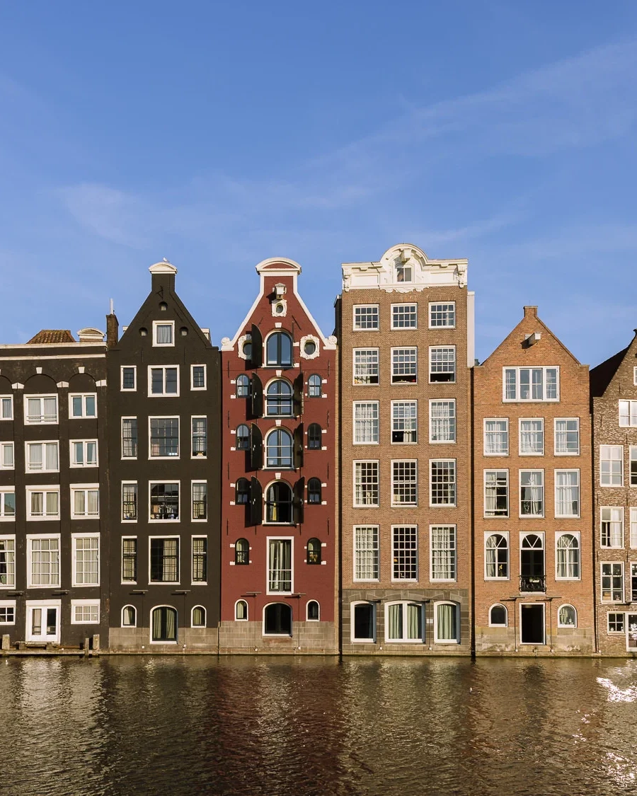Row of narrow historic canal houses along a waterfront in Amsterdam