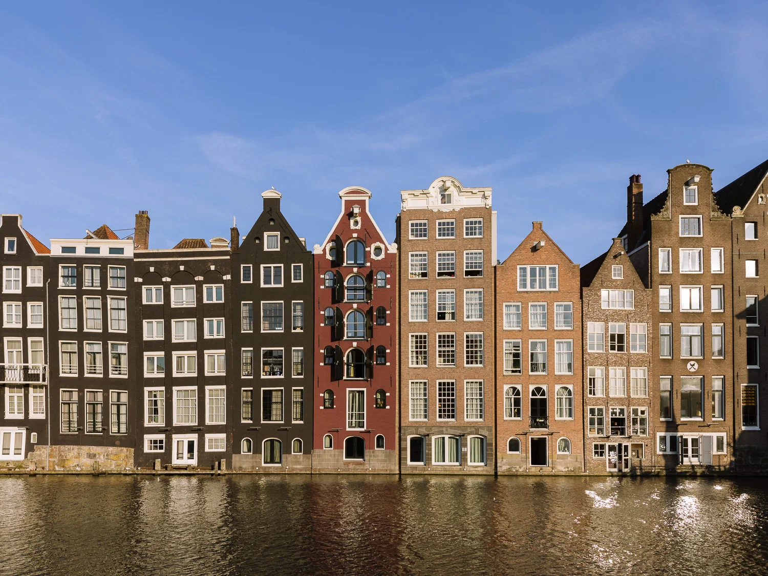Row of narrow historic canal houses along a waterfront in Amsterdam