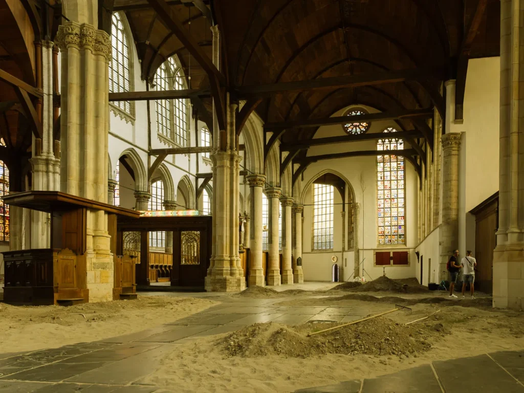 Pale stone columns, stained-glass windows and dark wooden roof beams inside Amsterdam’s Oude Kerk, with mounds of earth covering the flagstone floor as part of Jesse Darling’s Godsworth installation