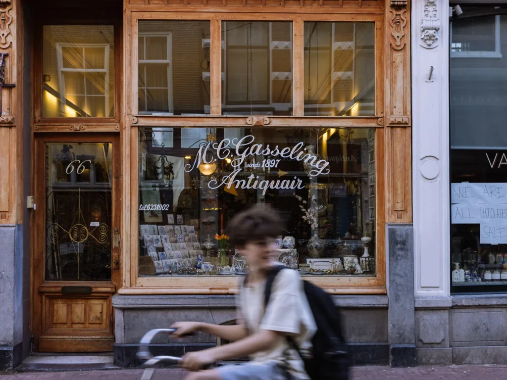Cyclist passing the window of M.C. Gasseling Antiquair on Nieuwe Spiegelstraat in Amsterdam