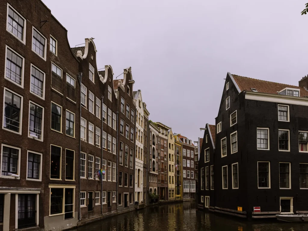 Tall, narrow canal houses in dark brick and painted façades line both sides of a quiet canal in central Amsterdam. 