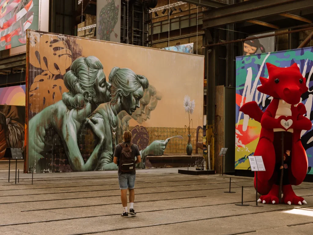 Visitor viewing large-scale street-art panels and a red dragon sculpture at STRAAT Museum in Amsterdam
